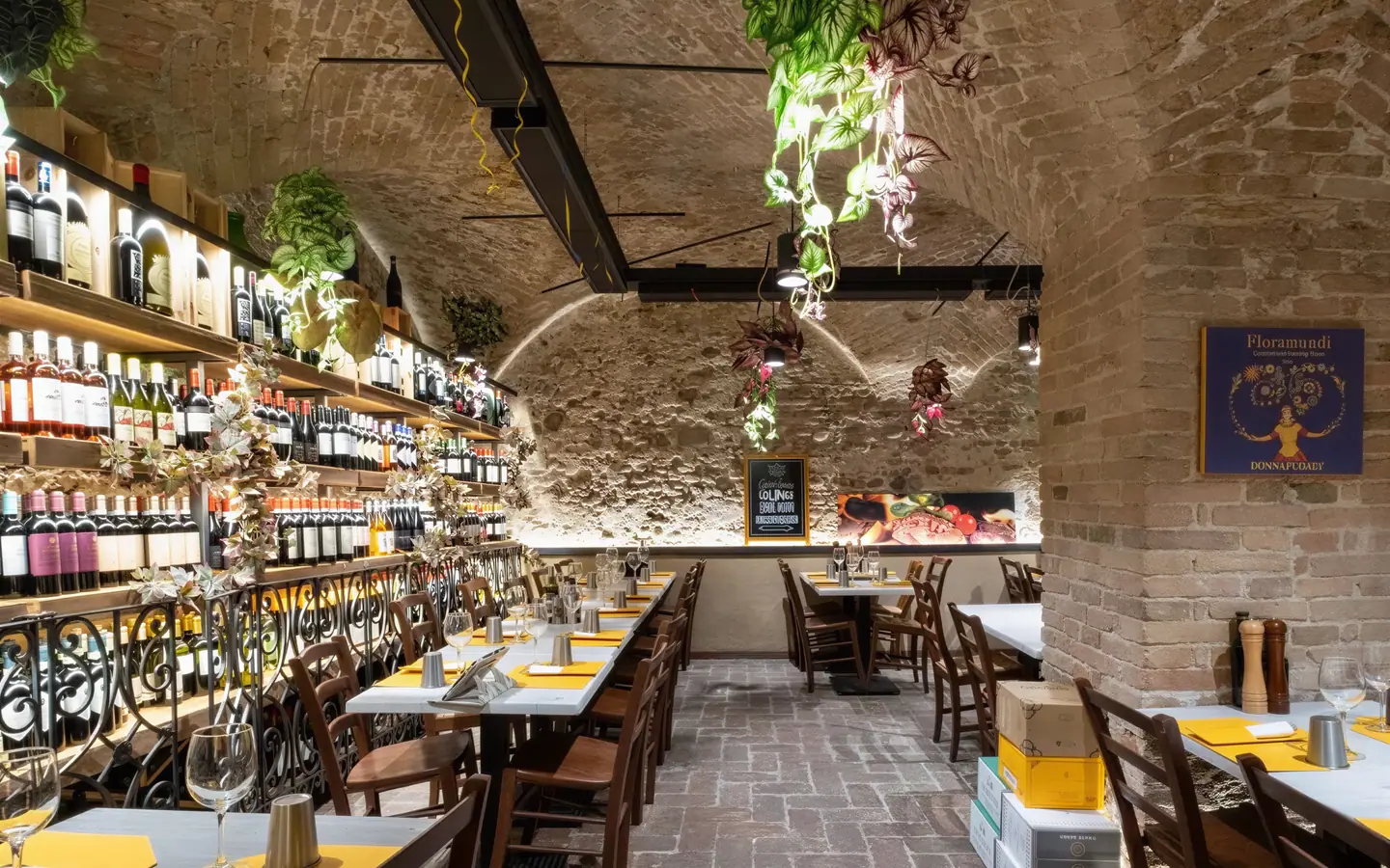 La sala della Piazzetta sotto le volte in mattoni, con le pareti di bottiglie, le piante sospese e i tavoli apparecchiati – Verona